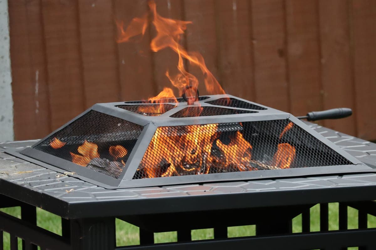 A square patio fire pit burning with a mesh spark-screen lid seated on top
