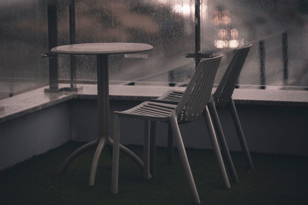 Plastic chairs and a table on a balcony in the rain
