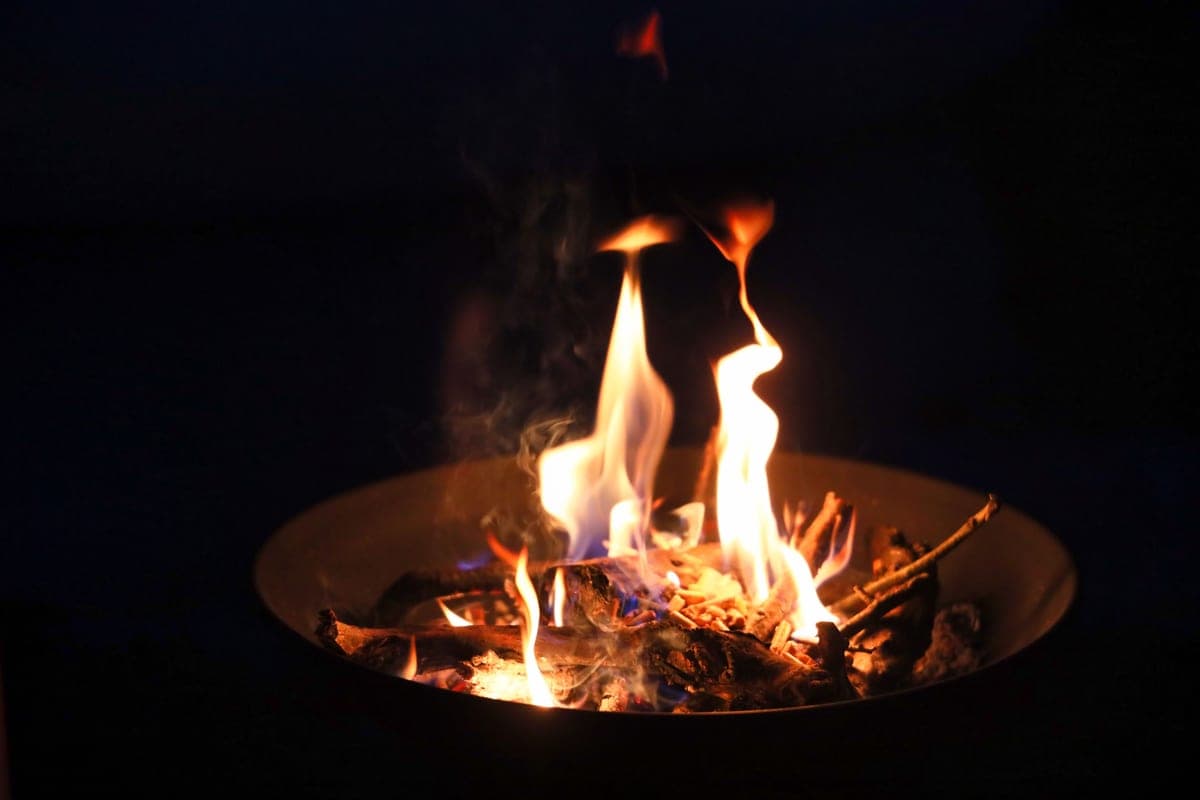 A smooth metal fire bowl burning wood at night