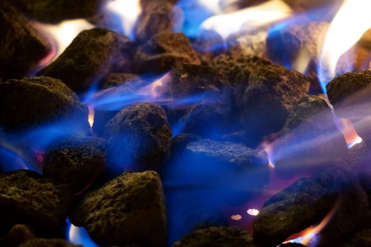 Blue gas flames rising between pieces of porous lava rock in a gas fire pit