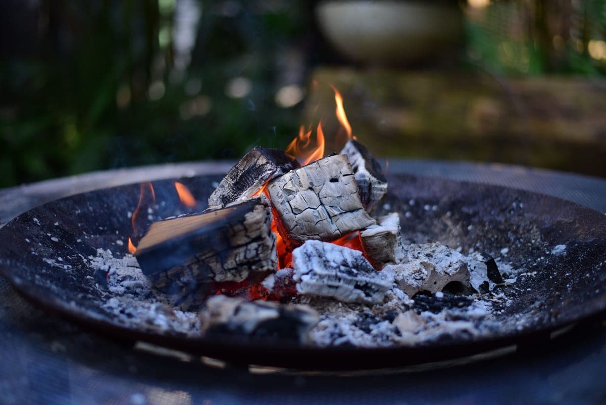 A shallow metal fire bowl with burning logs over a bed of ash