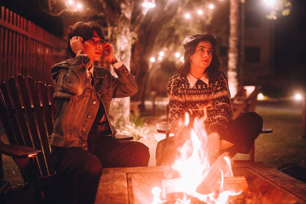 Two people sitting beside a lit backyard fire pit at night