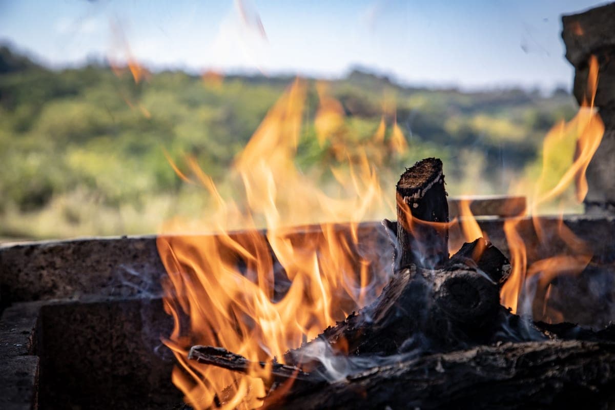 An open wood fire burning in a stone pit, thin smoke drifting across the flames