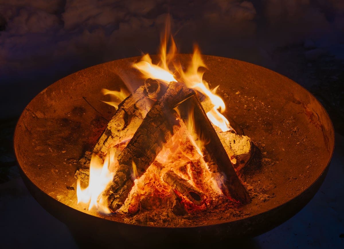 A shallow steel fire bowl with a wood fire burning at dusk