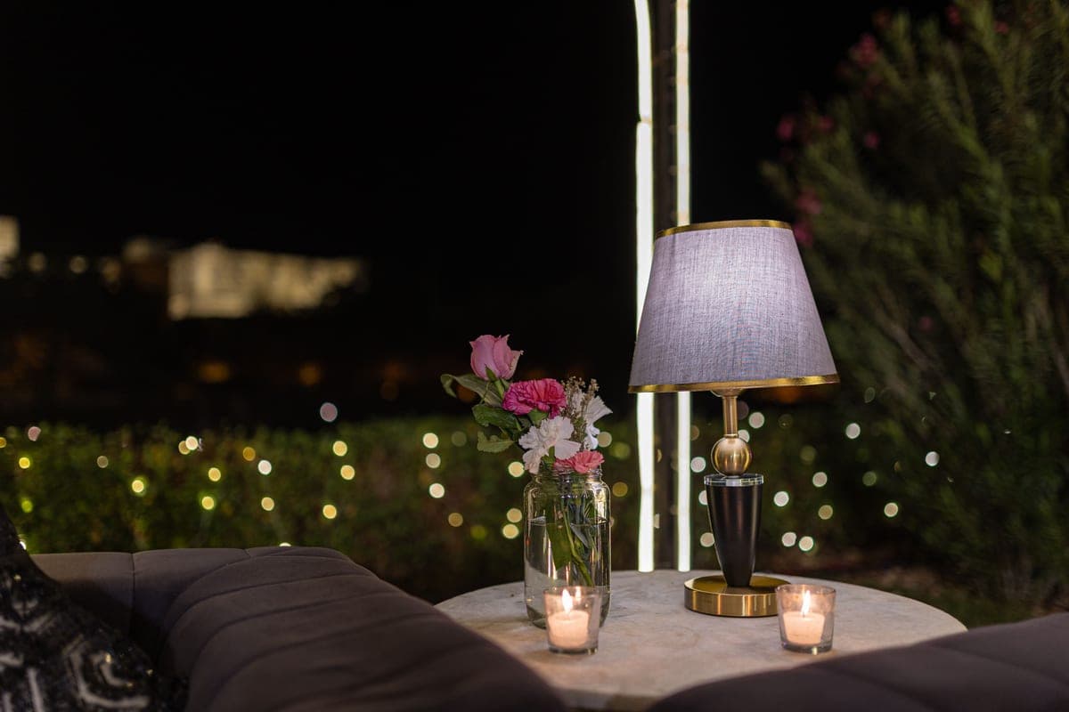 An outdoor garden table with flowers and a lamp in the evening